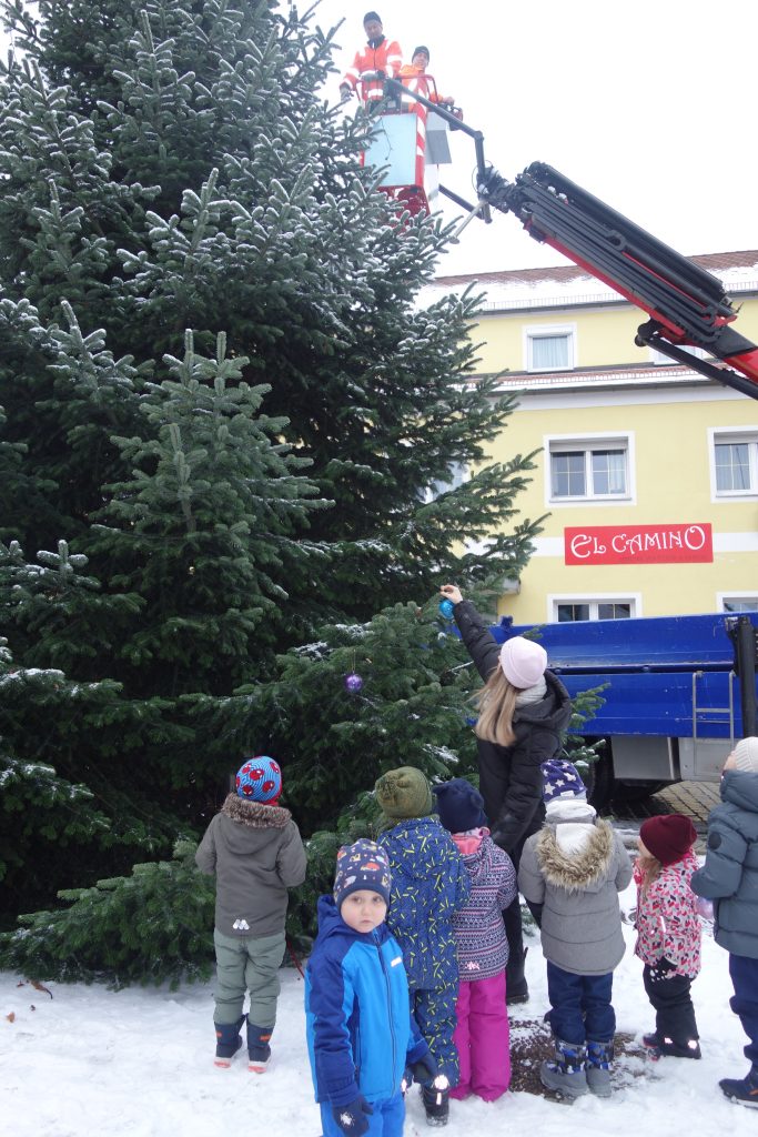 Wir hängen unsere selbst gebastelten Kugeln an den Baum am Marktplatz. Bürgermeister Hr. Teplitzky und einige Stadtmitarbeiter helfen uns dabei.