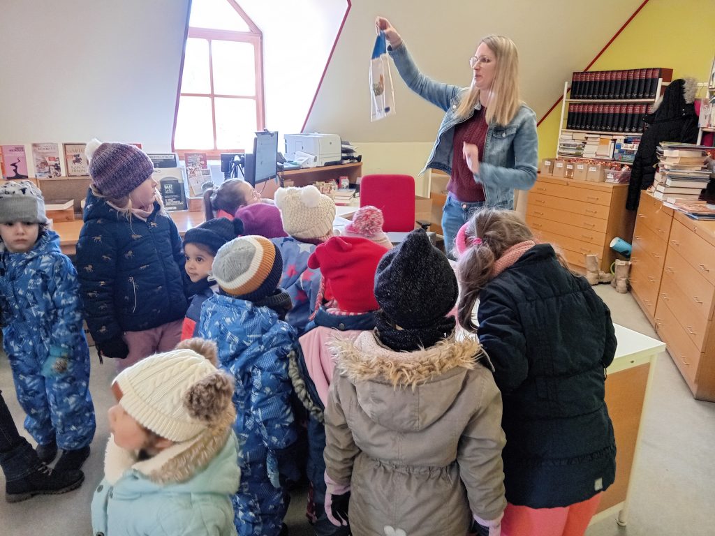 Wir besuchen die Bücherei. Frau Hagl überreicht der Katzengruppe eine Büchertasche.